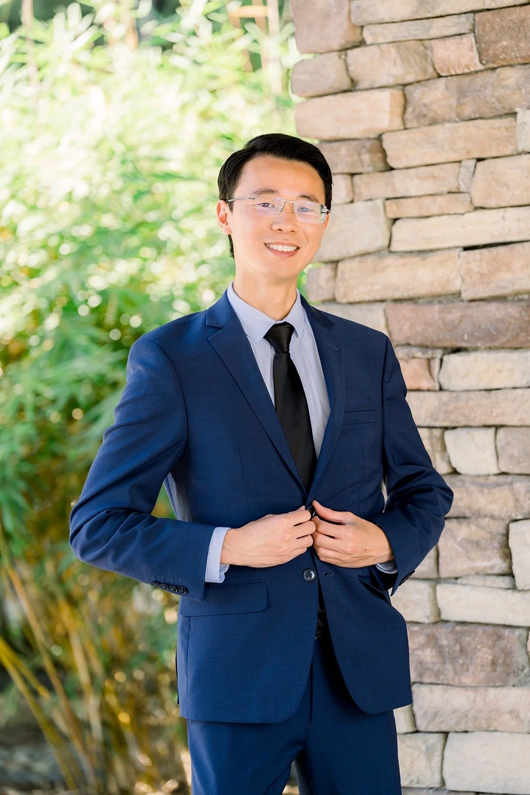 Alex buttoning his navy jacket beside a stone pillar