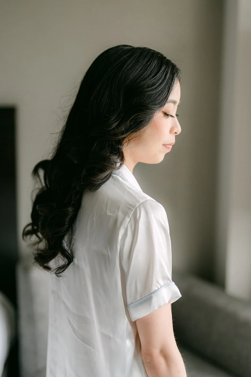 Natalie in her robe with her hair done in long soft curls, looking toward the window light