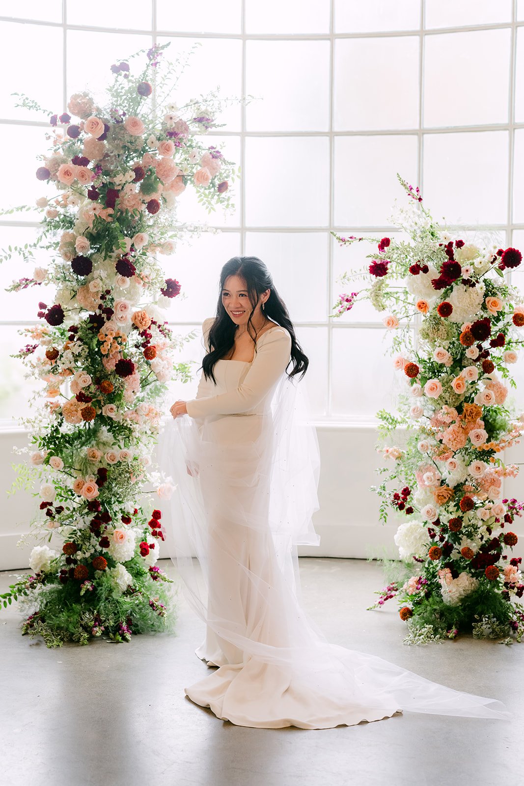 Denise standing between the floral columns in front of the window wall.
