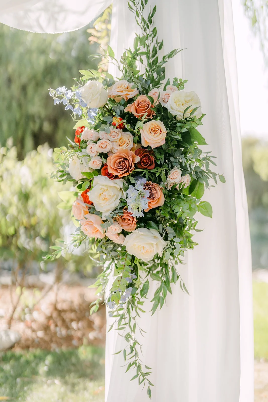 Peach rose and greenery arrangement on the draped ceremony arch