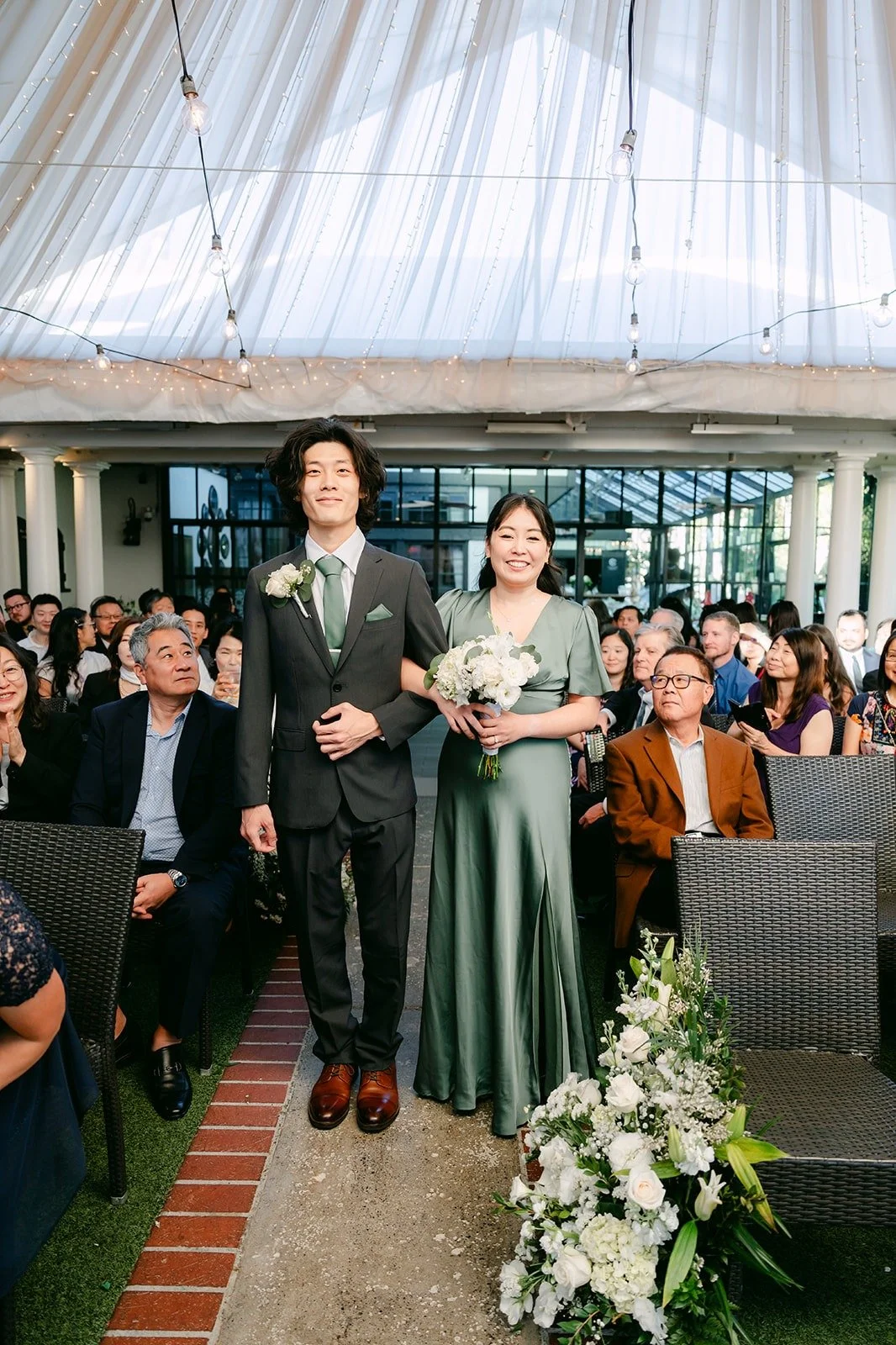 A bridesmaid in sage green and a groomsman walking down the aisle