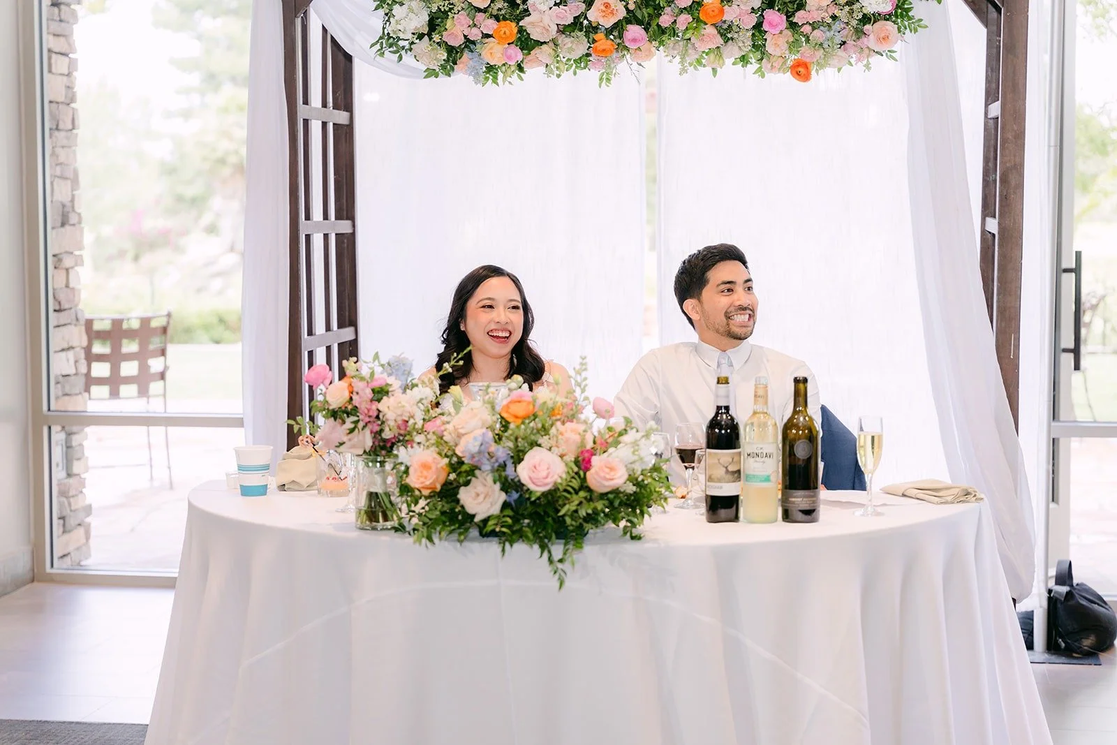 Natalie and Mark listening from the sweetheart table under the floral arch