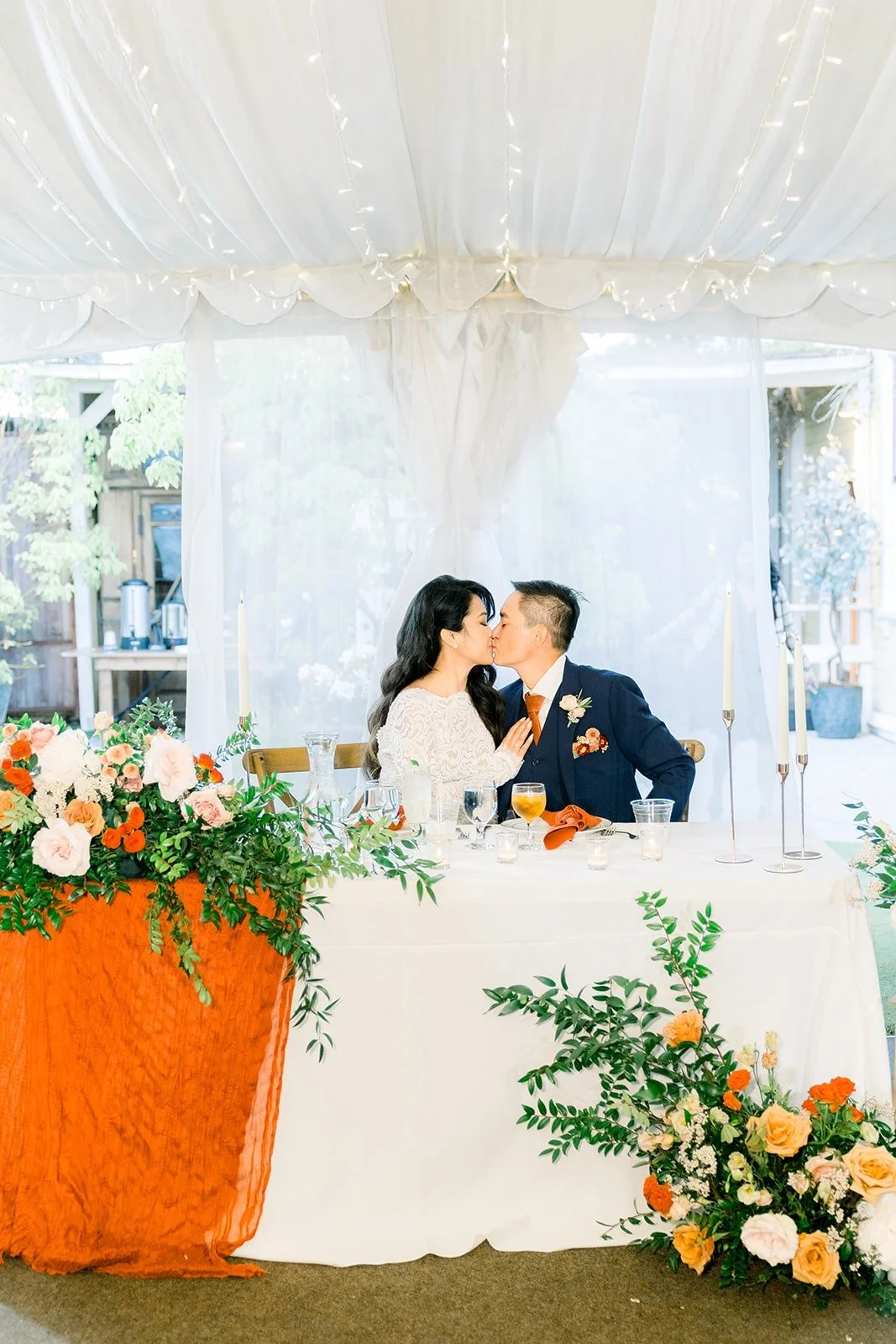 Hannah and Vincent at their sweetheart table with orange and blush florals