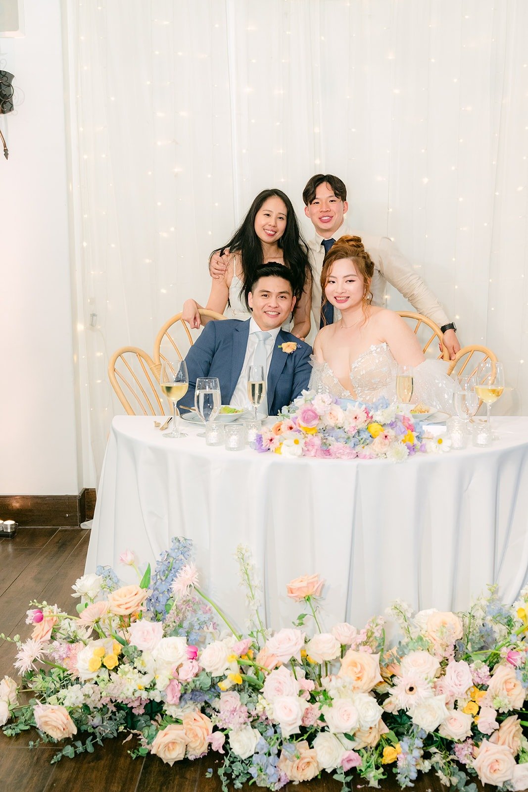 Joanna and Jerrick laughing at their sweetheart table with friends leaning in