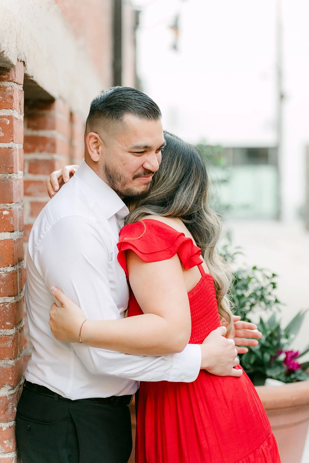Ankush hugs Linh tight beside the brick building.