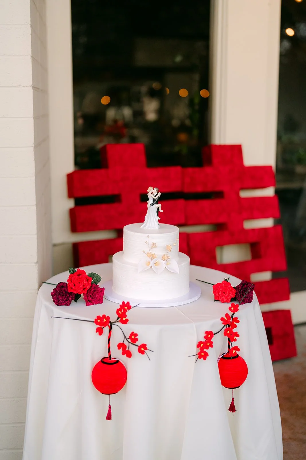 Wedding cake beside a red double happiness sign and tassels.
