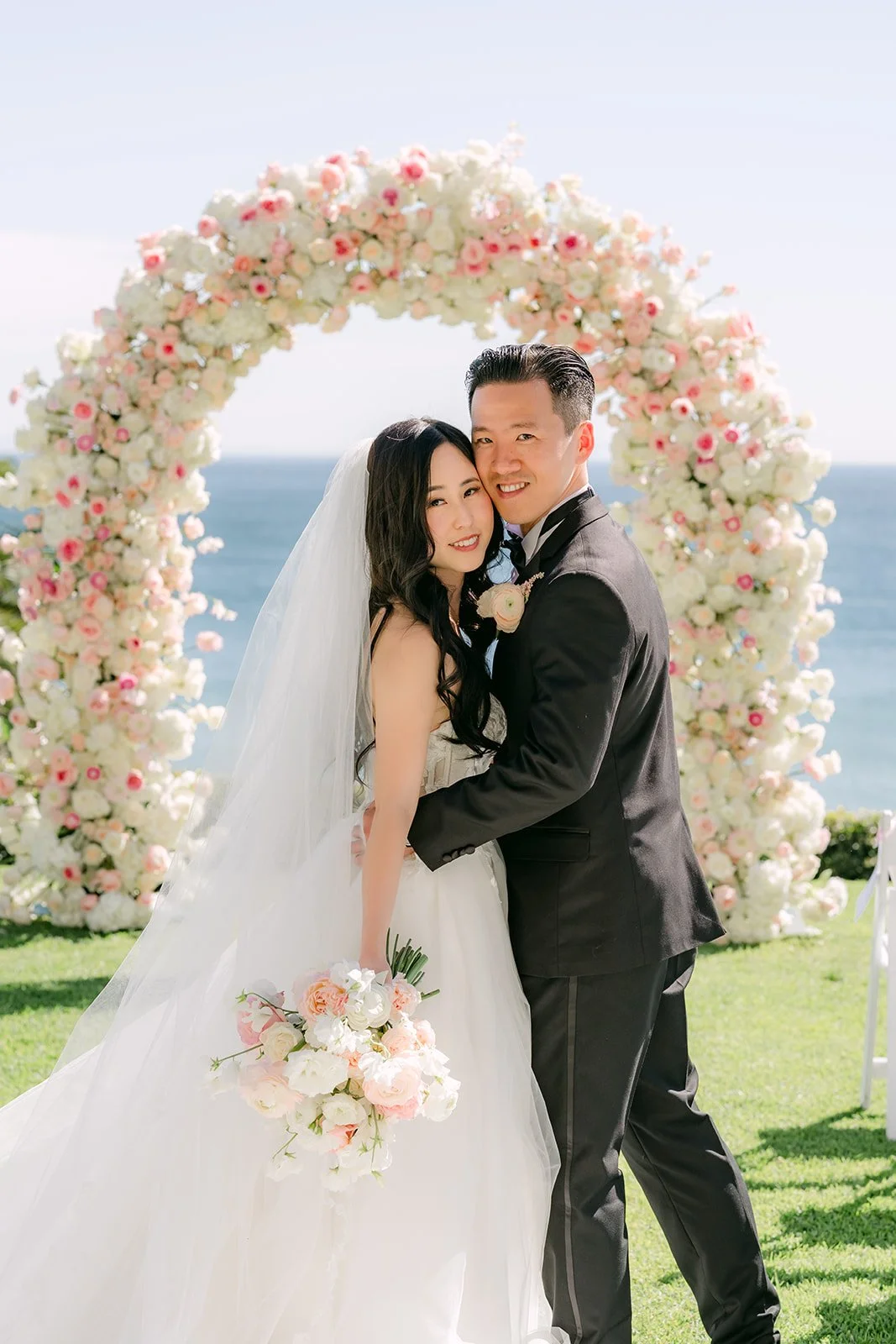 Kai hugging Kelley under the floral ceremony arch