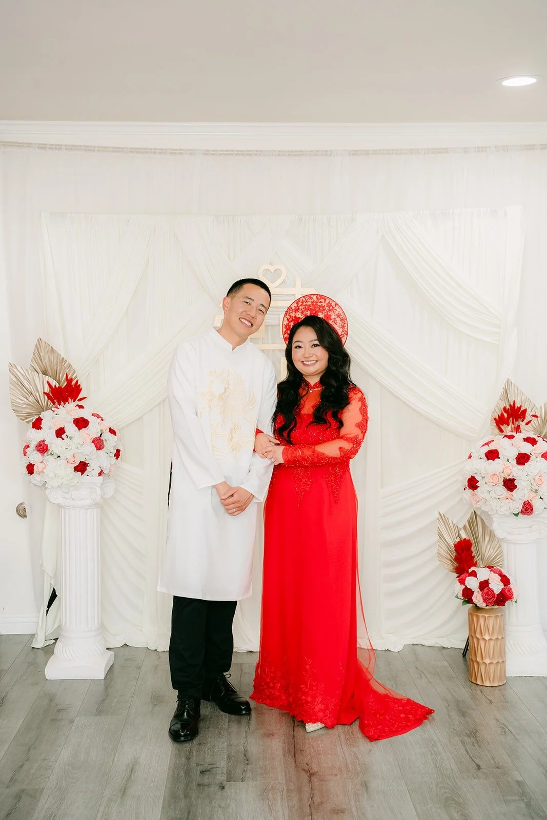 Jennifer and Kevin stand together in their ao dai in front of the white draping