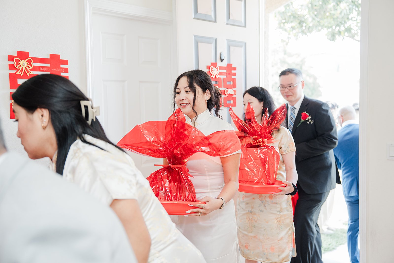 Bridesmaids receiving red gift trays at the door.