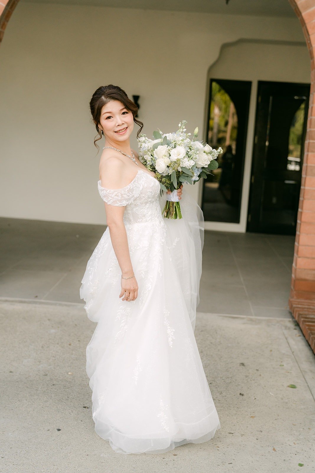 Sochi holds her white bouquet in the covered walkway at Sierra La Verne