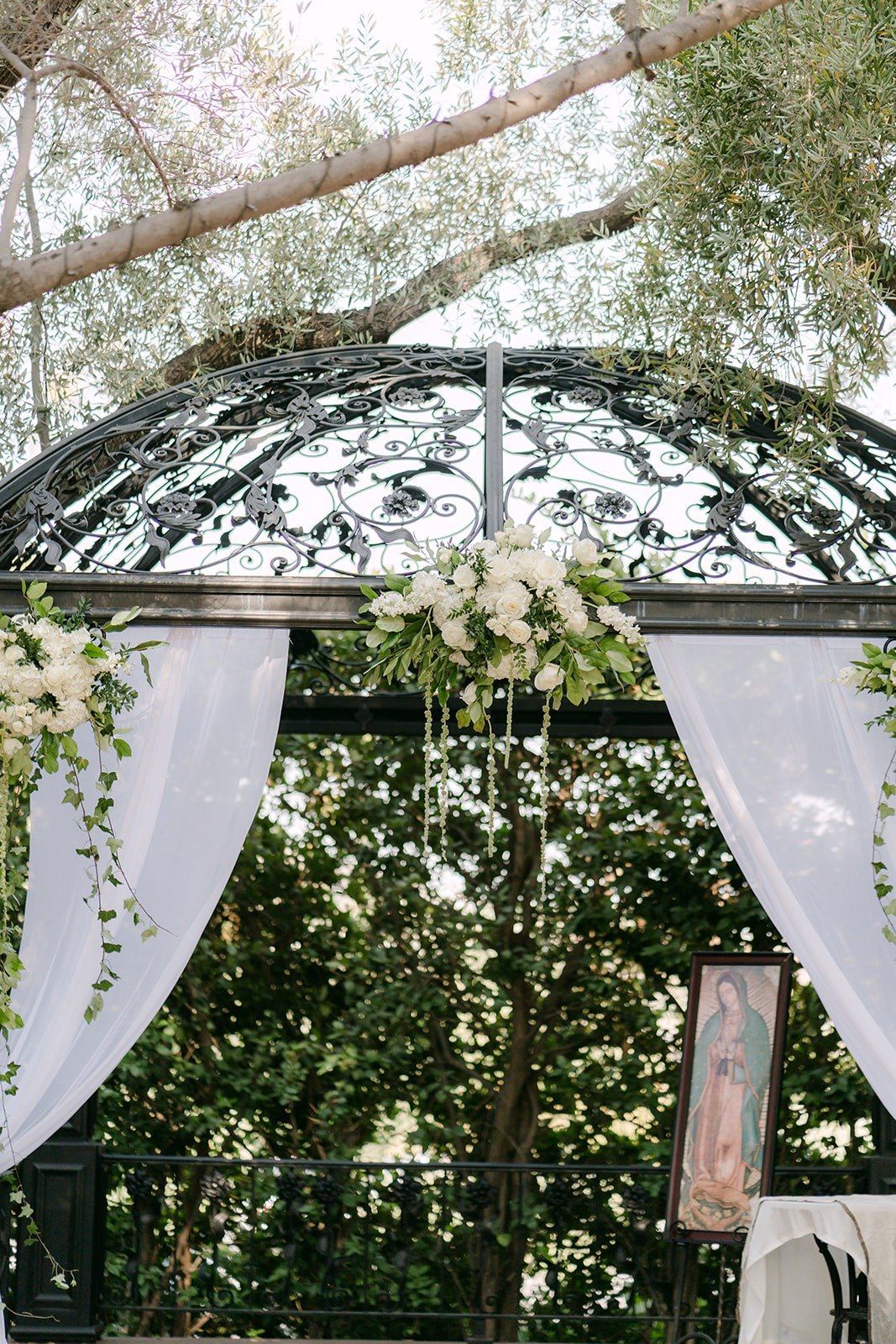 The wrought iron gazebo draped in white fabric with white florals