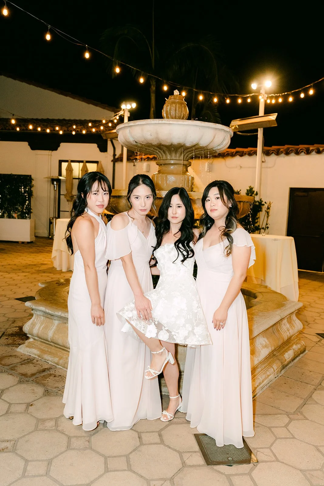 Bride and bridesmaids at the lit courtyard fountain at night