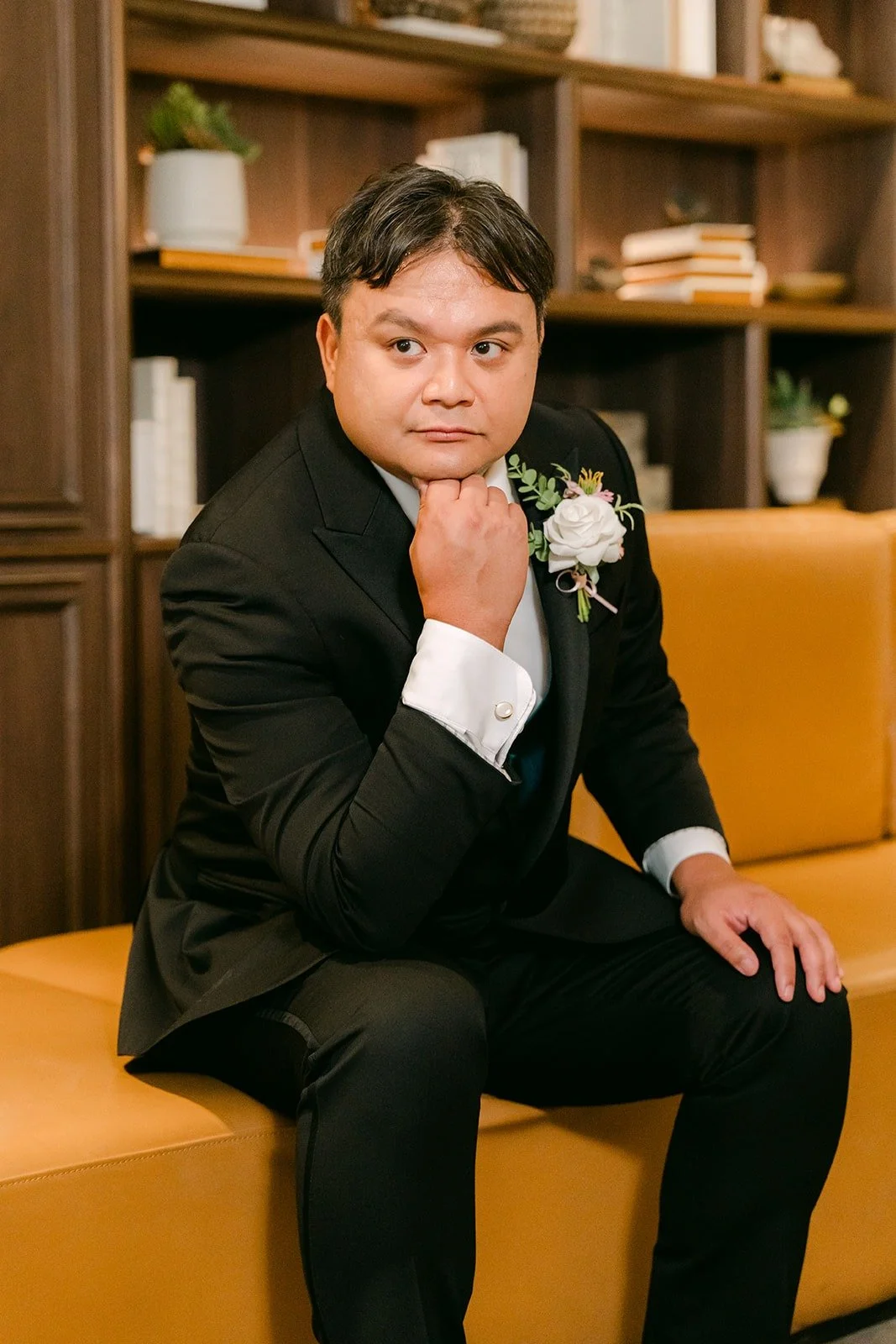 James sitting on an orange leather sofa in his black tuxedo, resting his chin on his hand