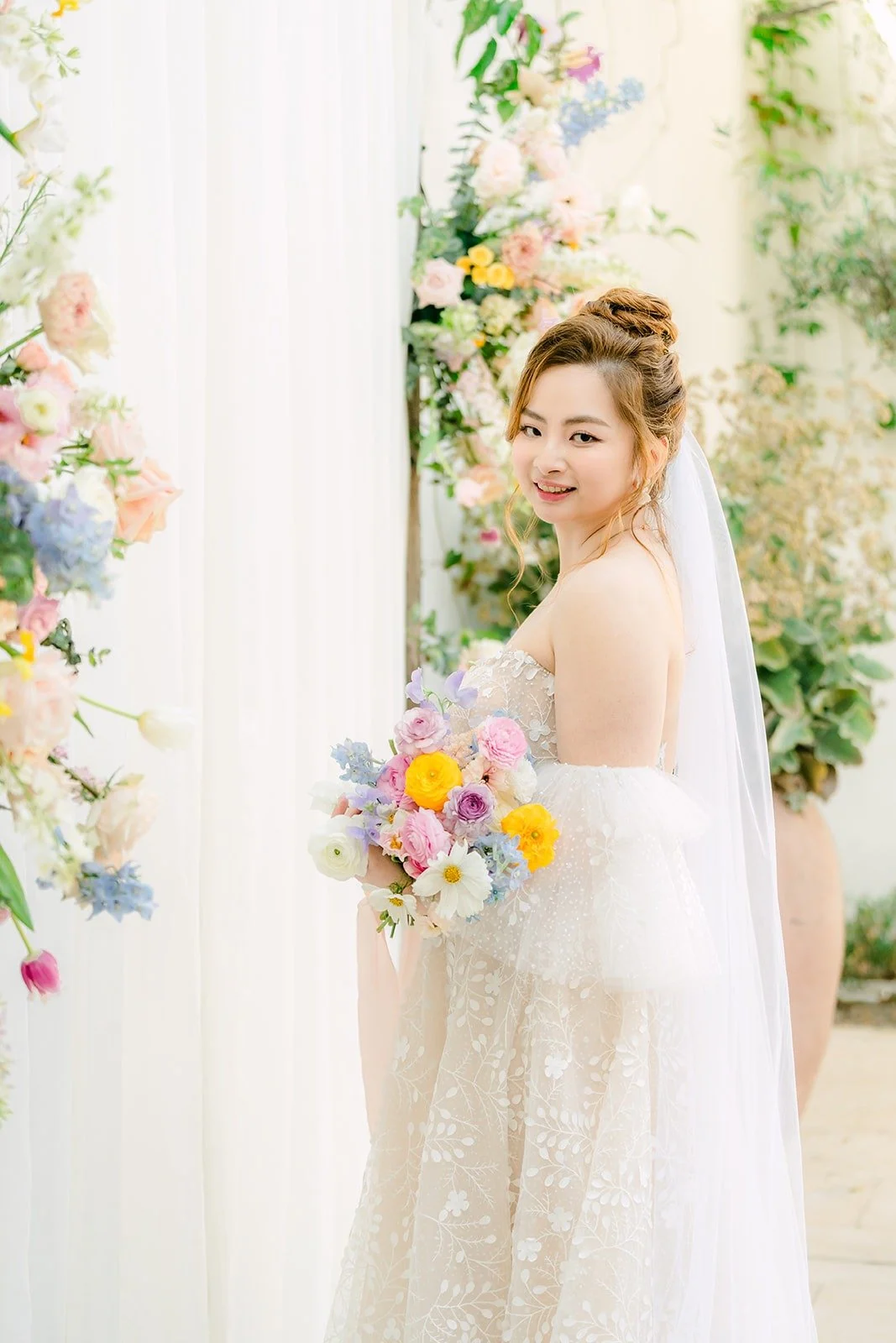 Joanna with her veil and pastel bouquet against the white wall