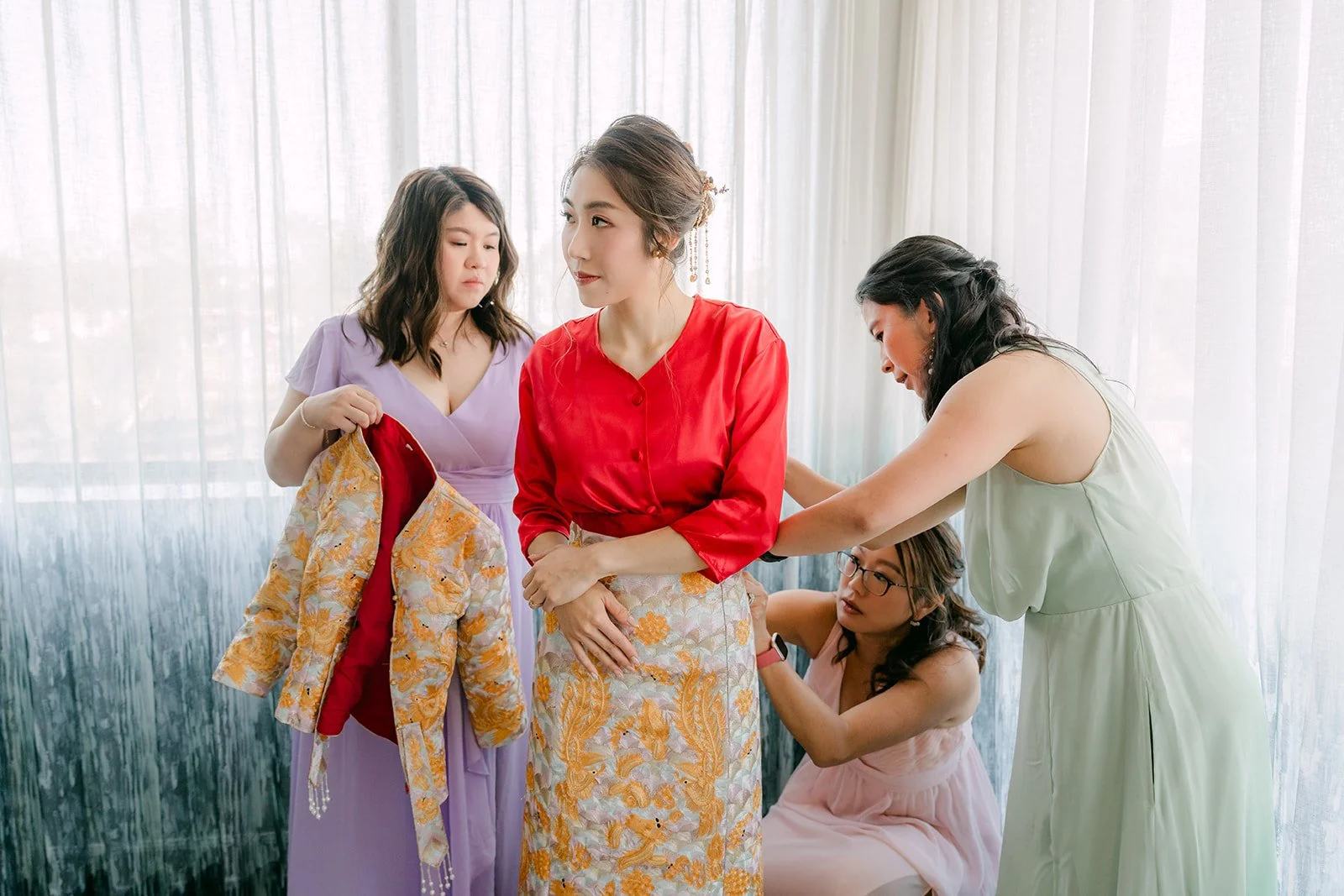 Christie's bridesmaids help fasten her qun kwa by the window.