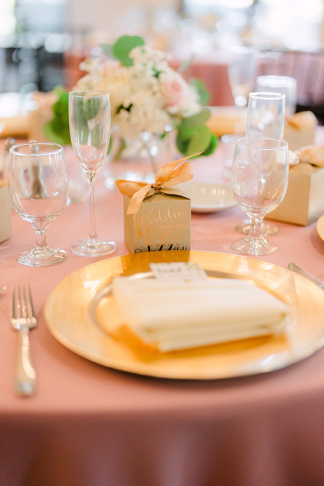 Gold chargers, blush linens and party favors at each place setting