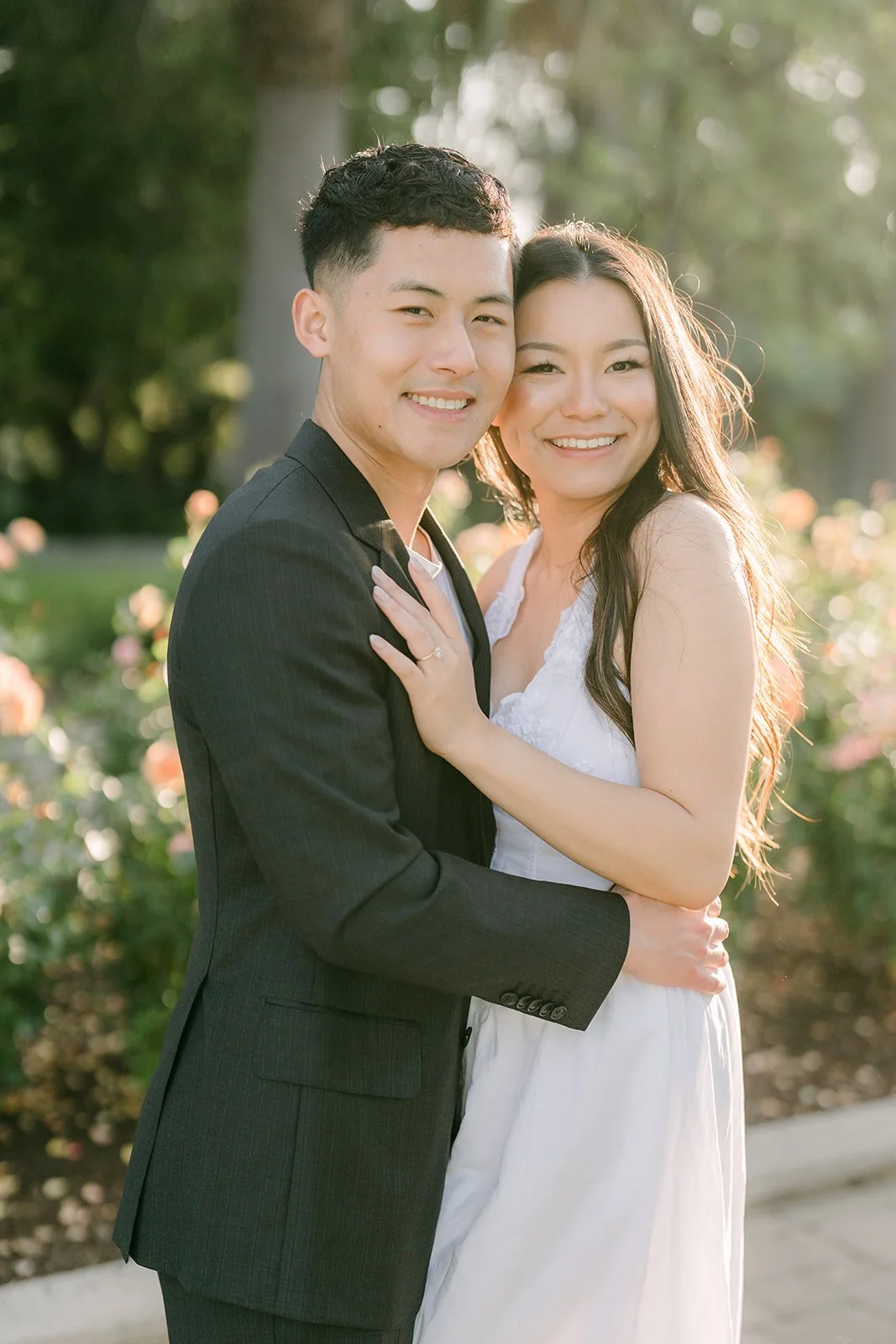 Richard in a black suit holds Jadee close in the park.