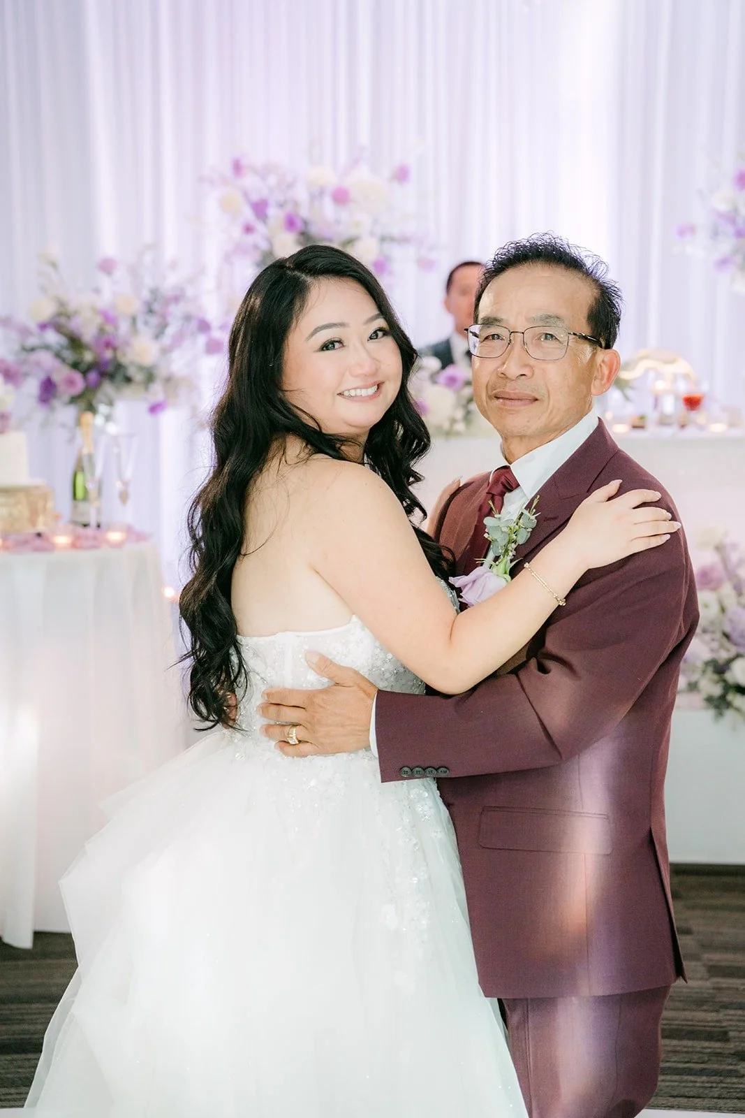 Jennifer smiles while dancing with a family member in a burgundy suit