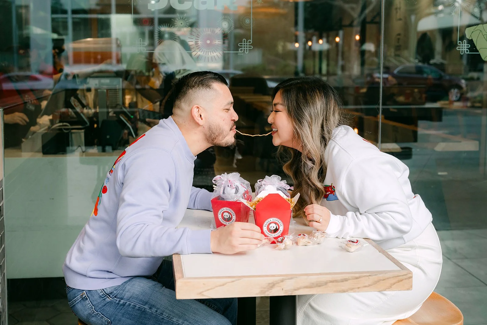 Linh and Ankush lean in for a kiss over their takeout boxes.