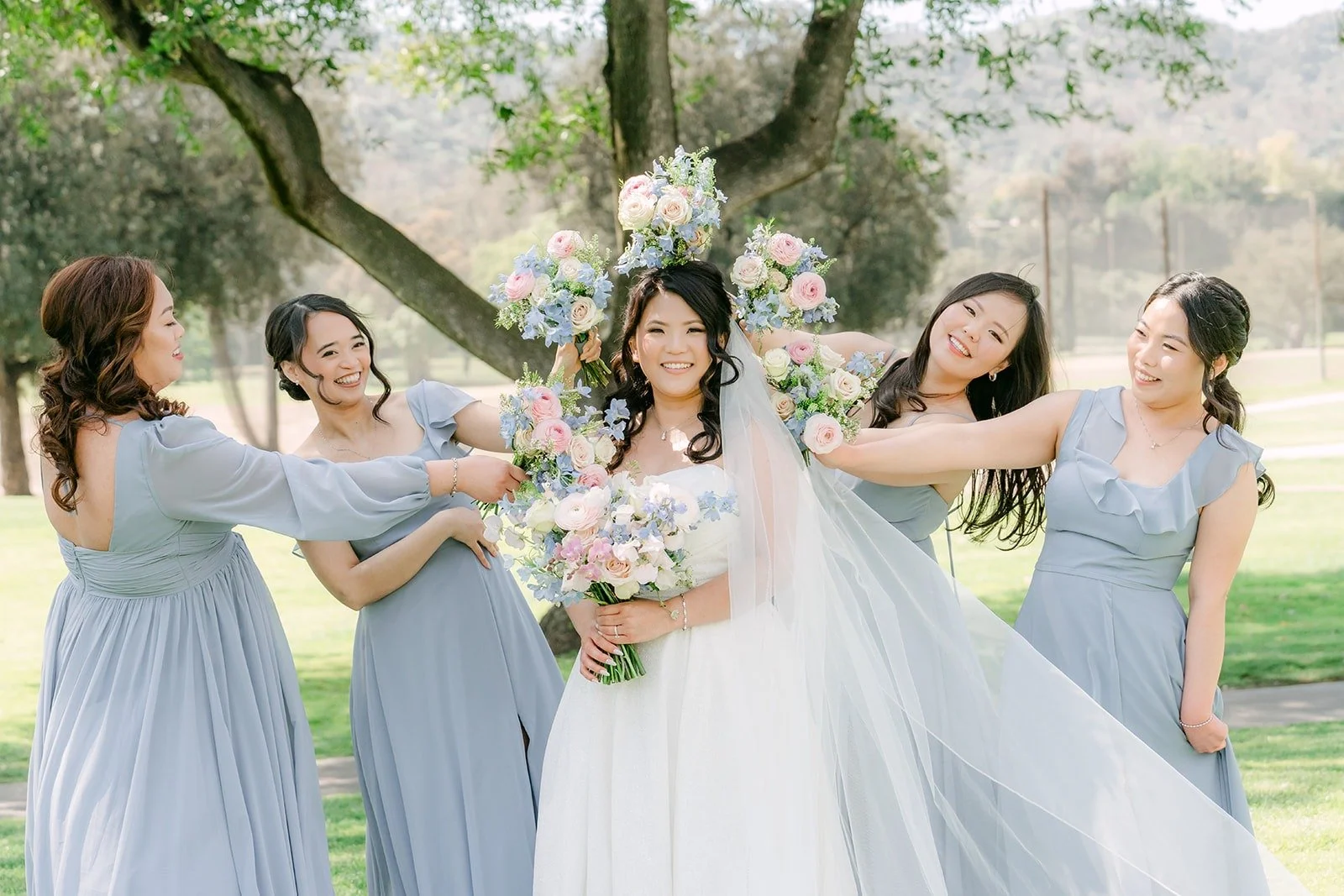 Bridesmaids in dusty blue gathering around Florence under the trees