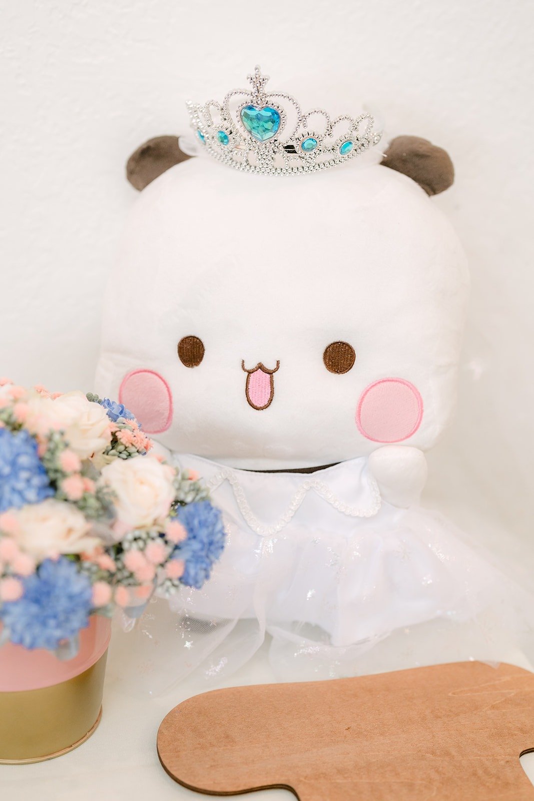 A plush bear in a tiara with white and blue flowers