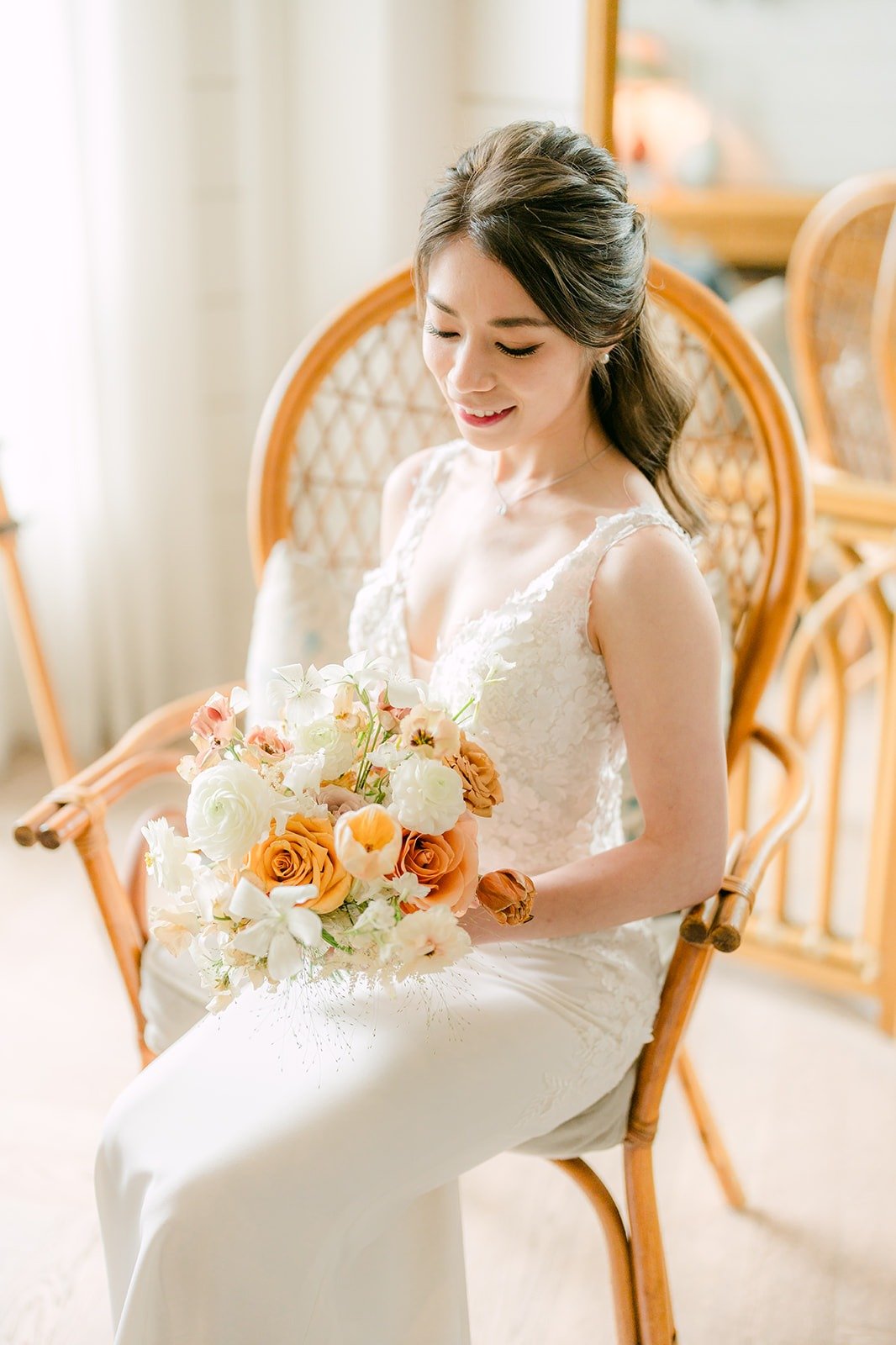 Angela seated in a rattan chair with her bouquet in her lace gown