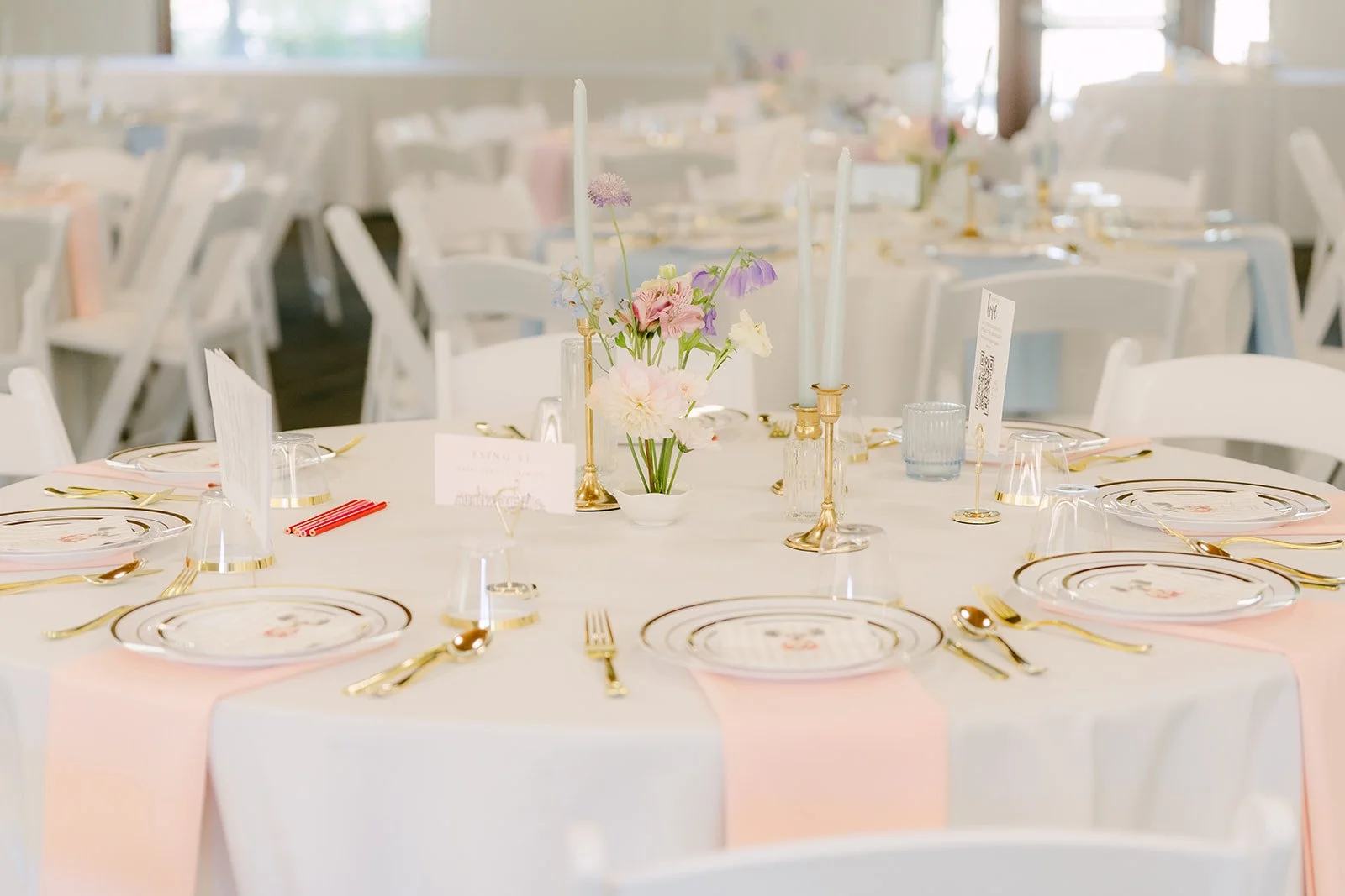 Round guest tables set with gold flatware and pastel napkins.