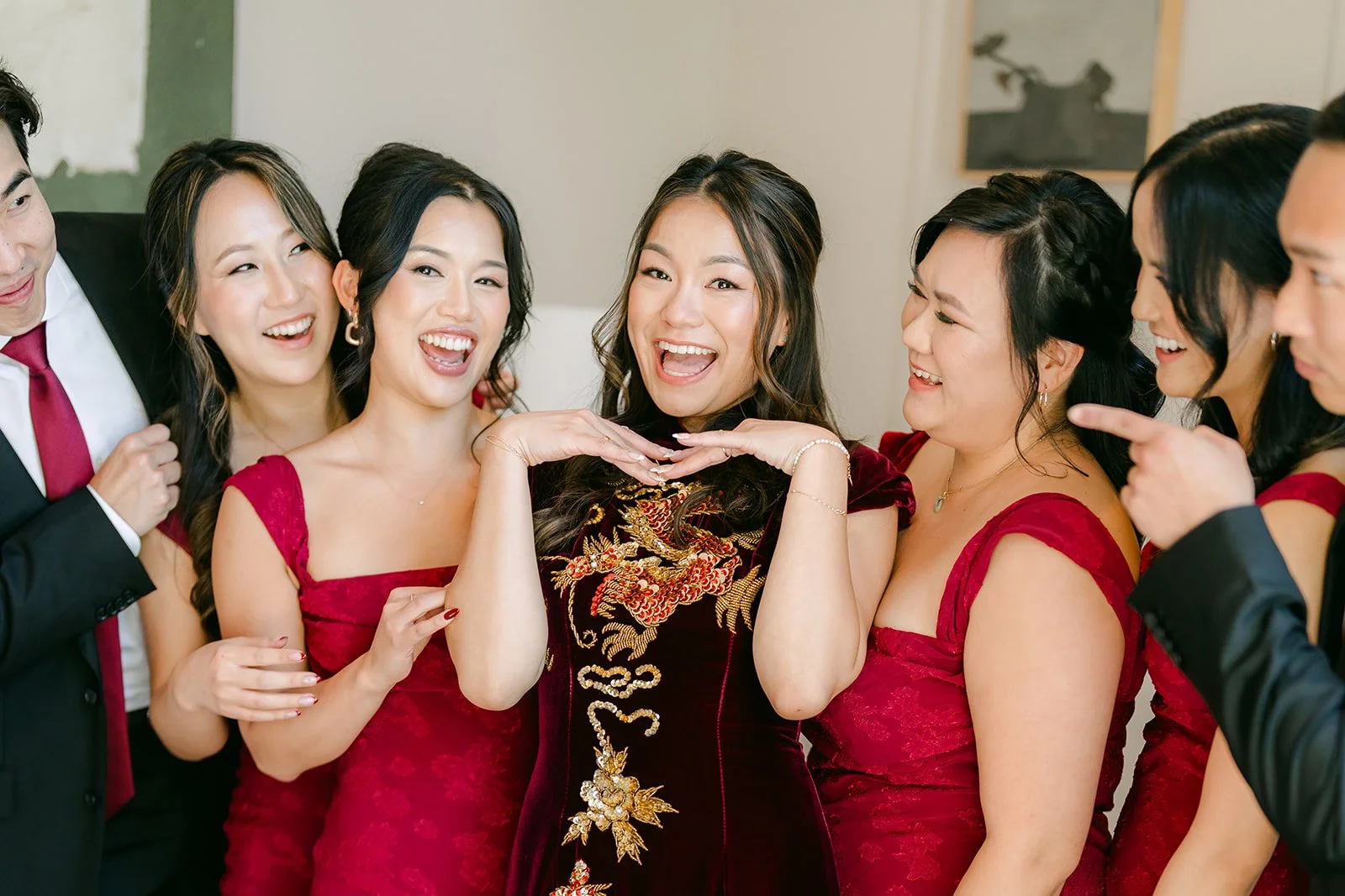 Bridesmaids in burgundy laughing with Jadee in her qipao