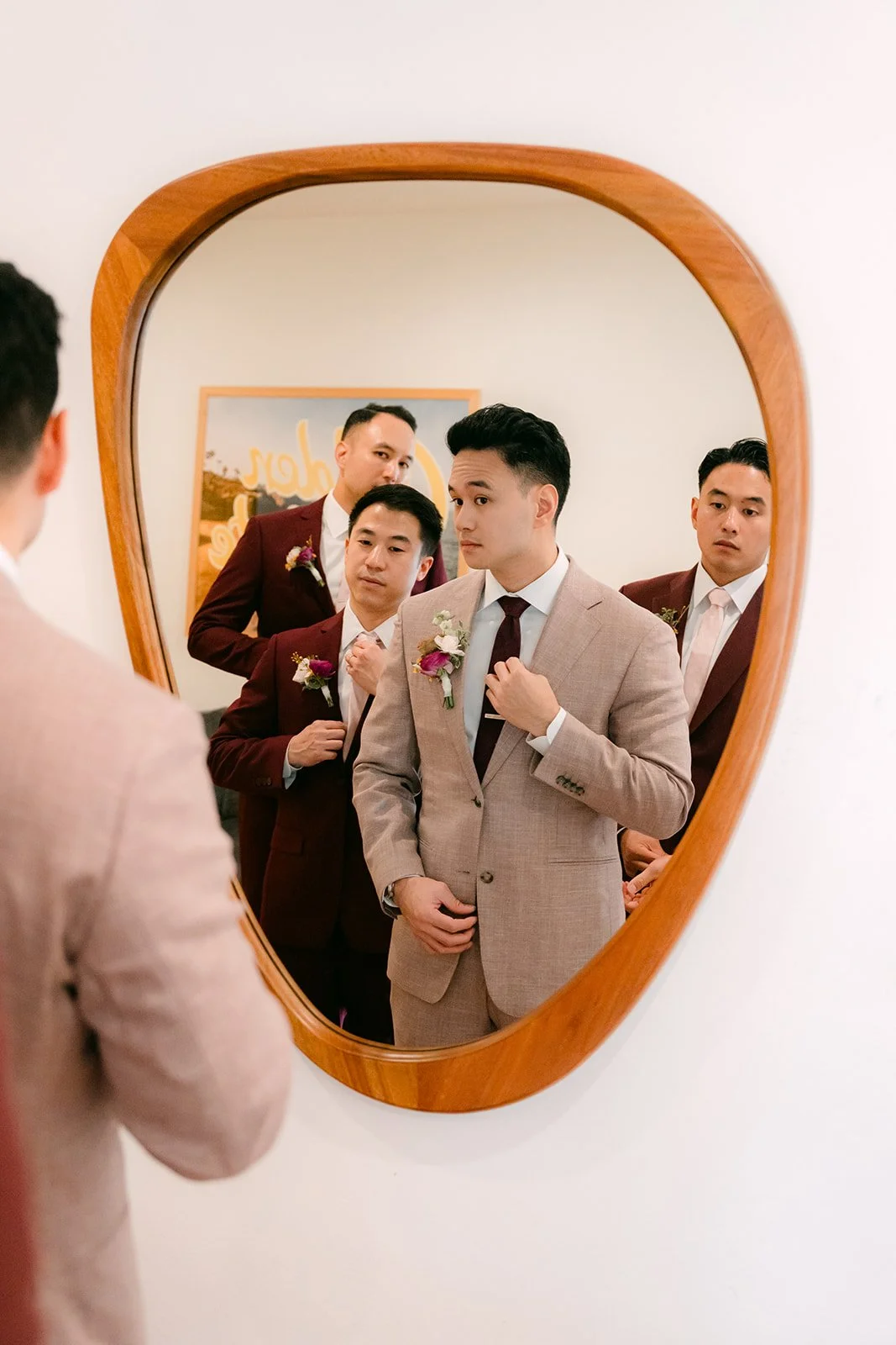 Michael and his groomsmen in burgundy suits reflected in a wavy mirror.