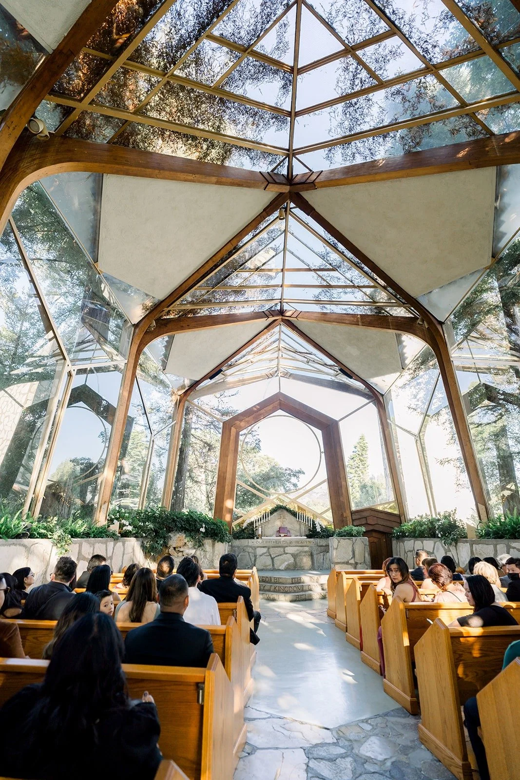 Guests fill the wooden pews under the glass roof of Wayfarers Chapel