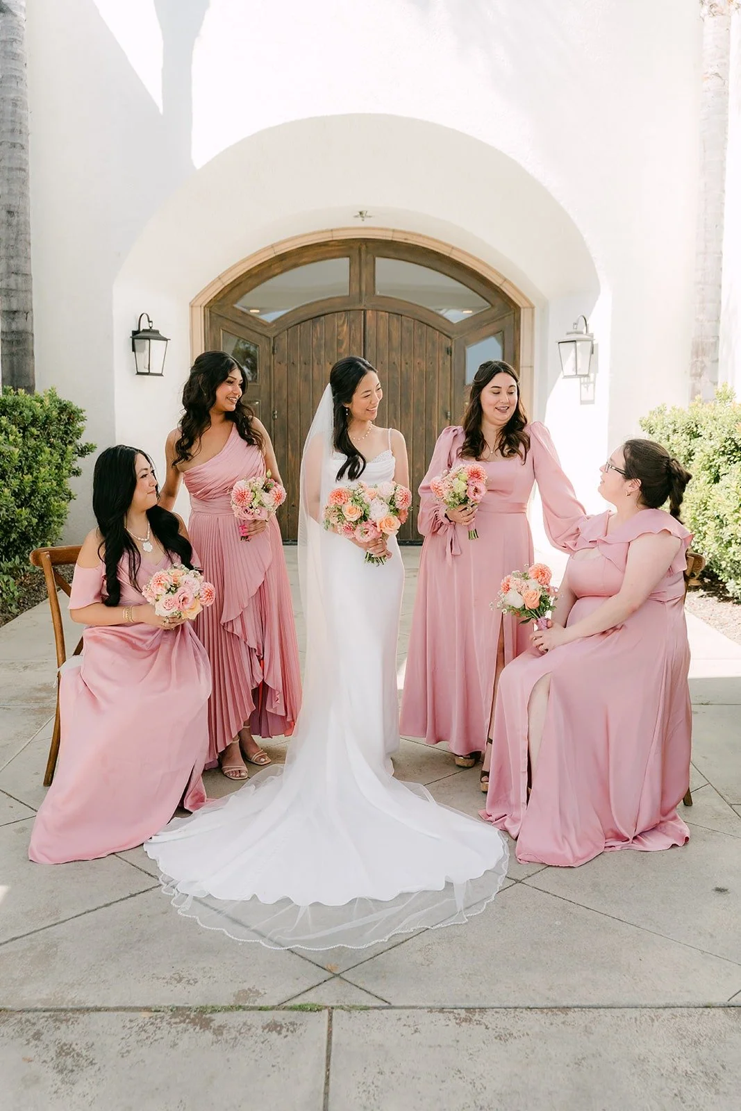 Stephanie and her bridesmaids seated in front of the arched wooden doors at Sterling Hills, photographed by One and Only Production