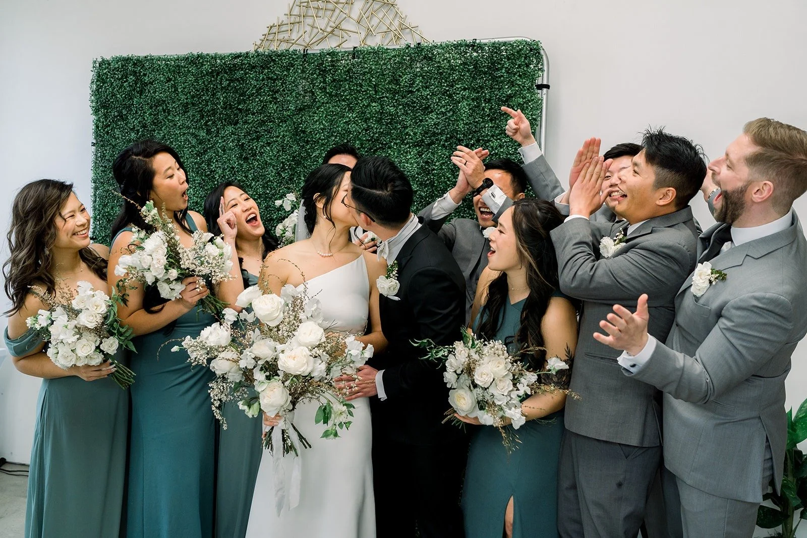 The wedding party in grey and sage green in front of the green hedge wall