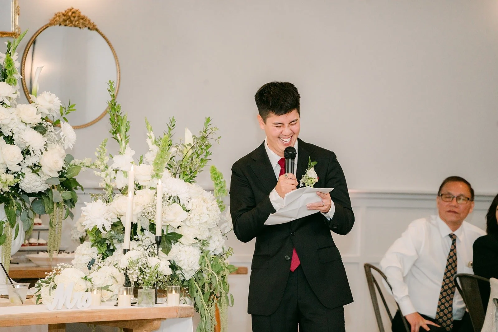 A groomsman reading his speech beside the white florals