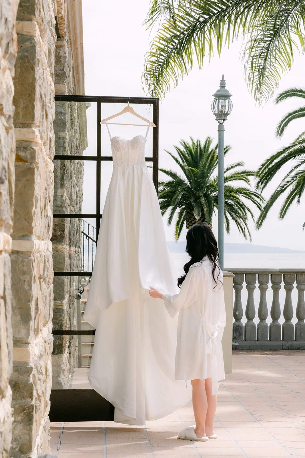 Wedding gown hanging in the doorway as the bride looks out at the palms