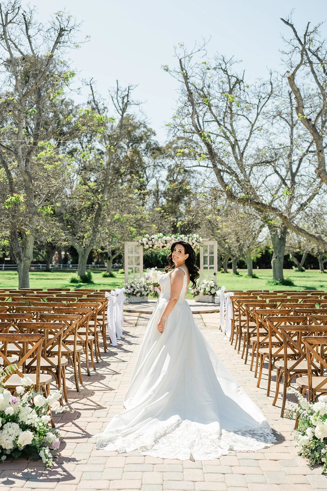 Bride standing in the ceremony aisle among the walnut orchard