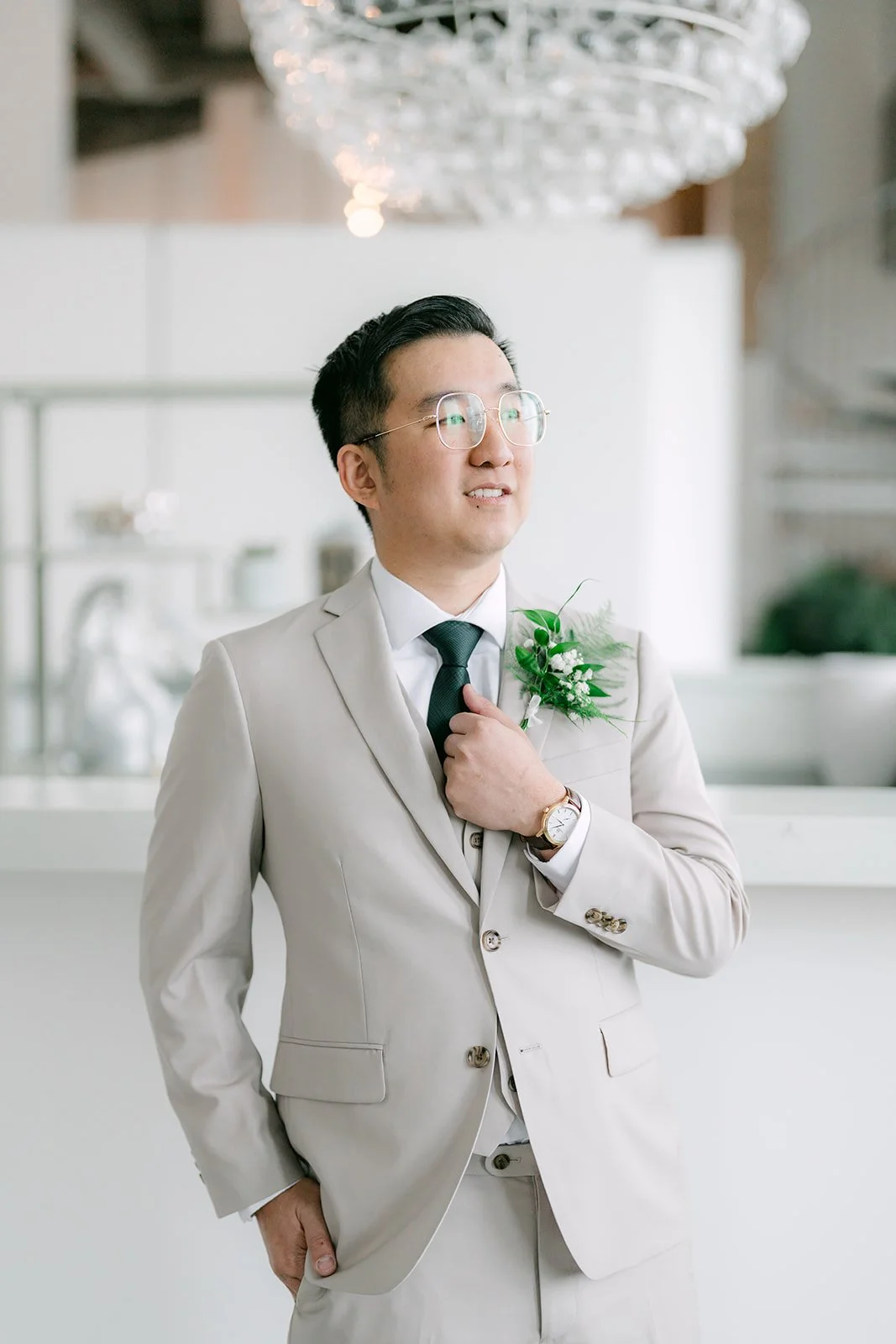 Groom adjusting his cufflinks under a crystal chandelier
