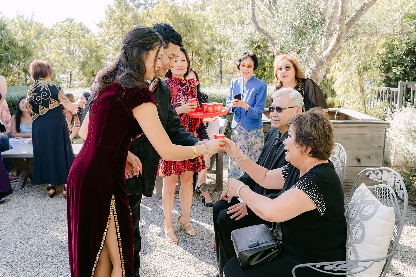 Jadee and Richard offering tea to seated relatives in the garden