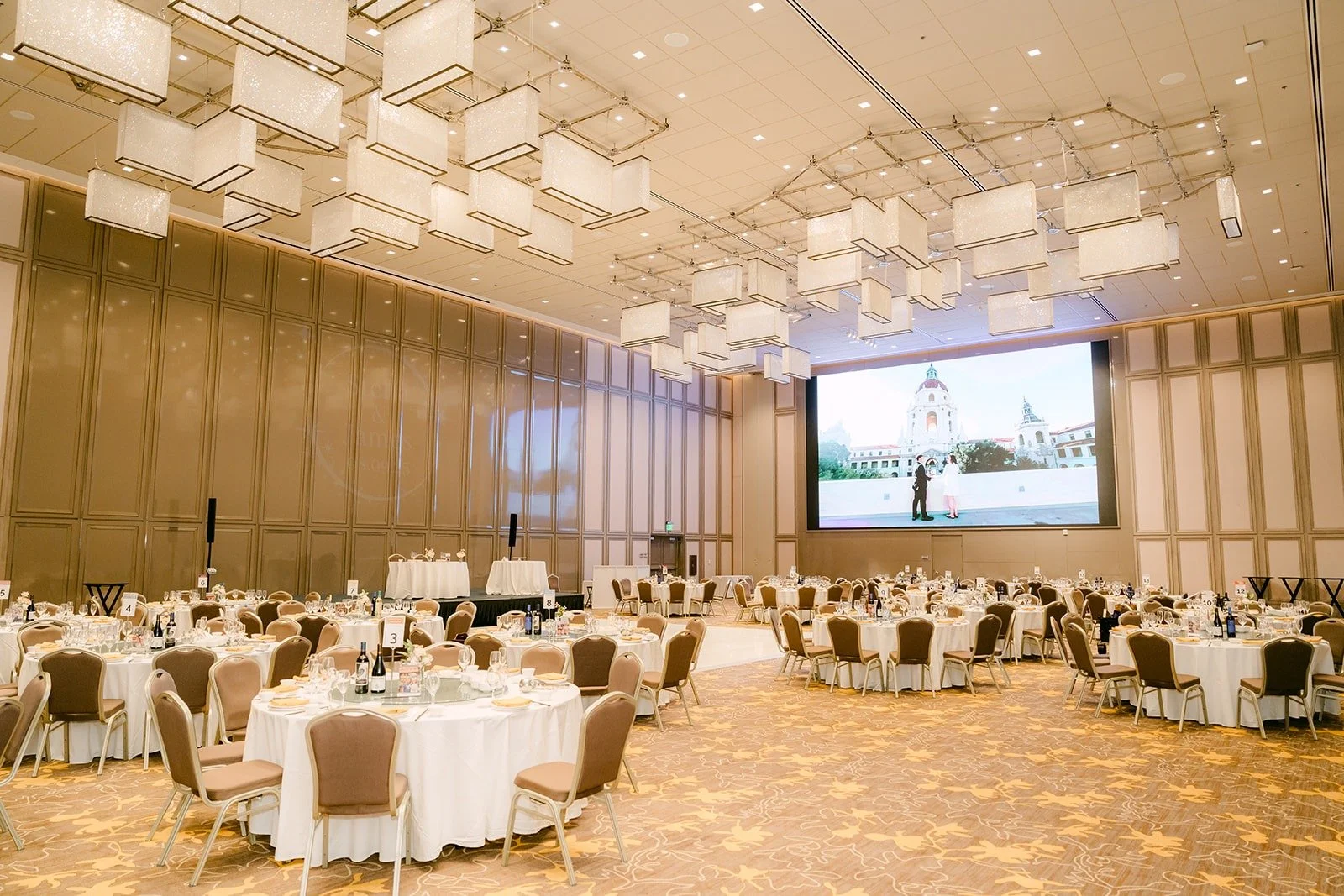 The ballroom set for the reception with round tables, white linens and a big screen
