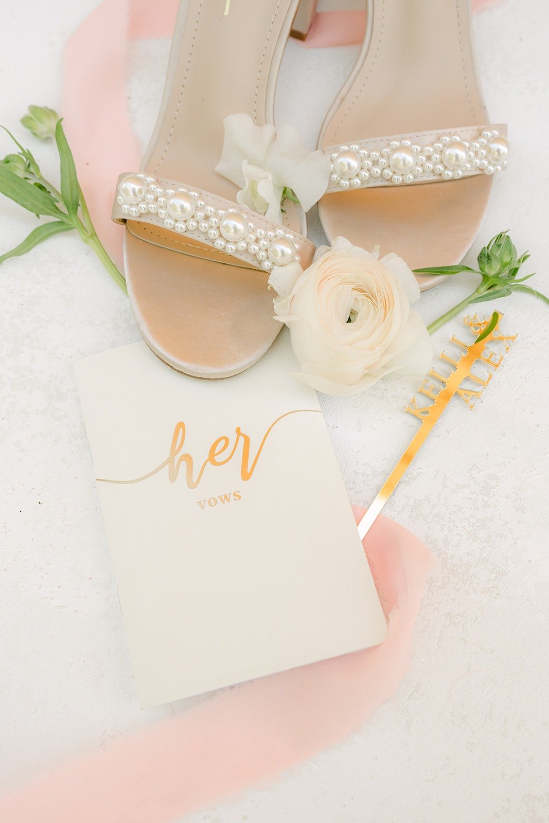 Kelli's sparkly heels next to a white vow book with gold lettering, photographed by One and Only Production