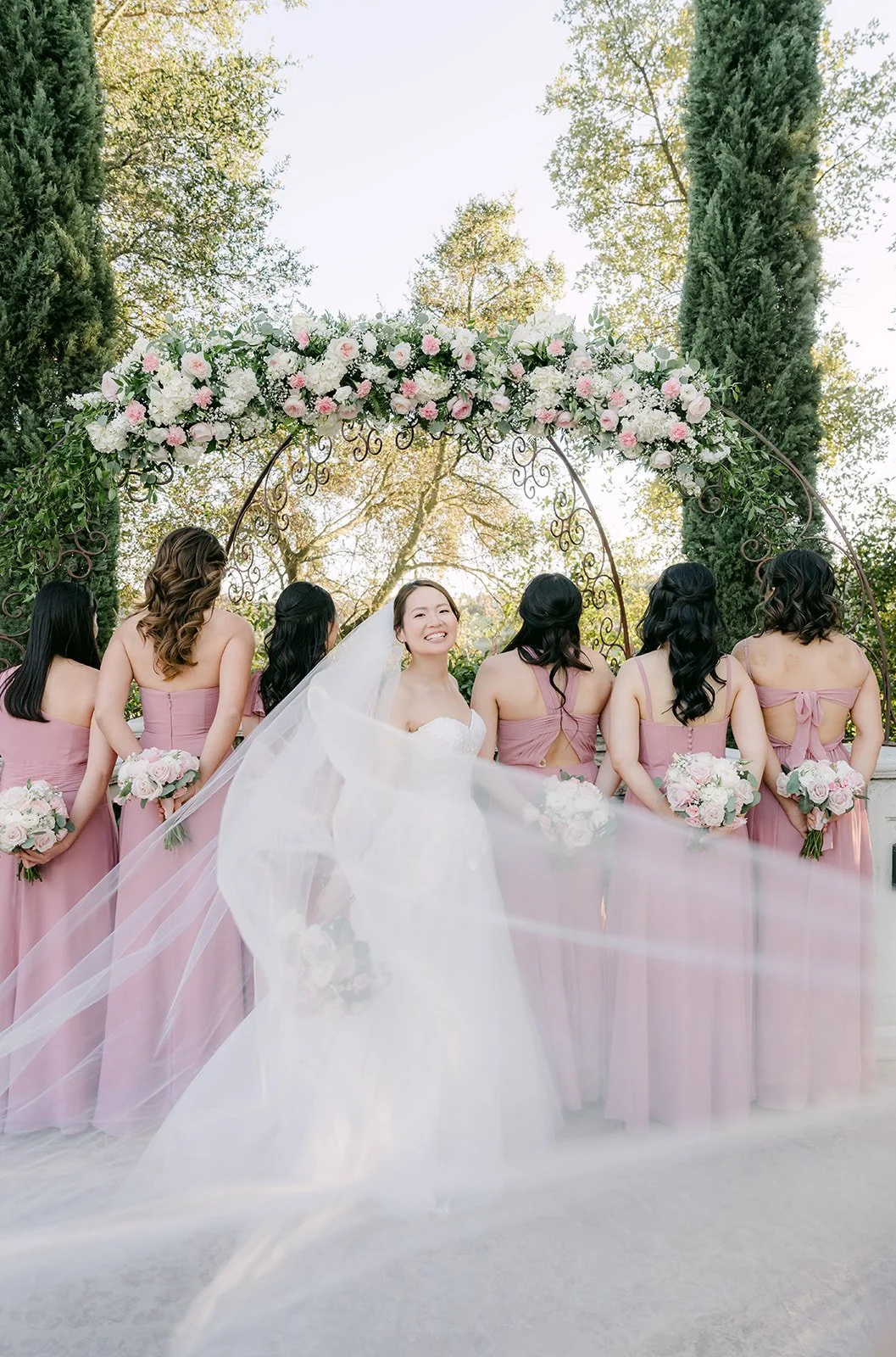 Bride's long veil flowing behind her as the bridesmaids look on