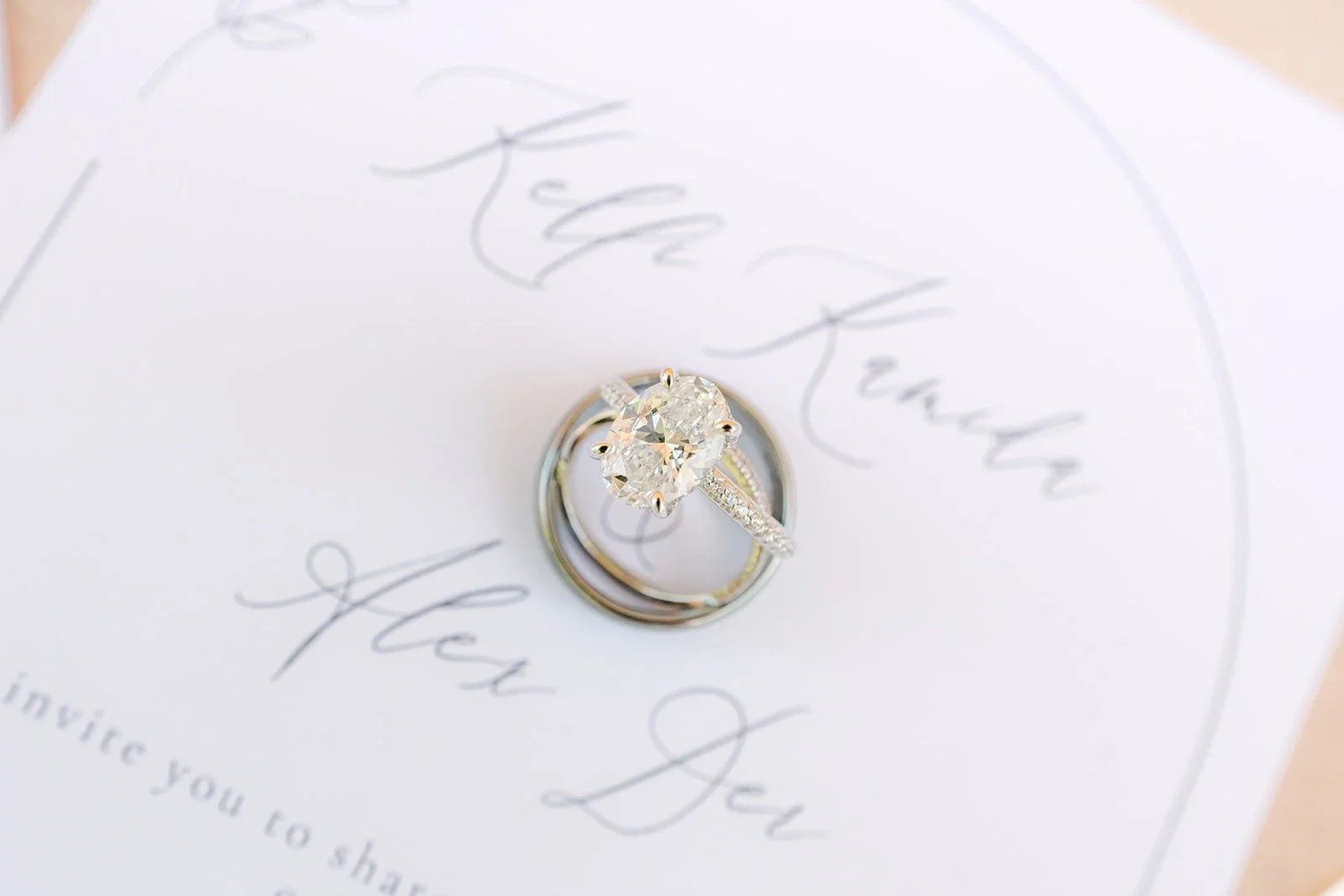 Kelli and Alex's wedding rings resting on the invitation with their names in script