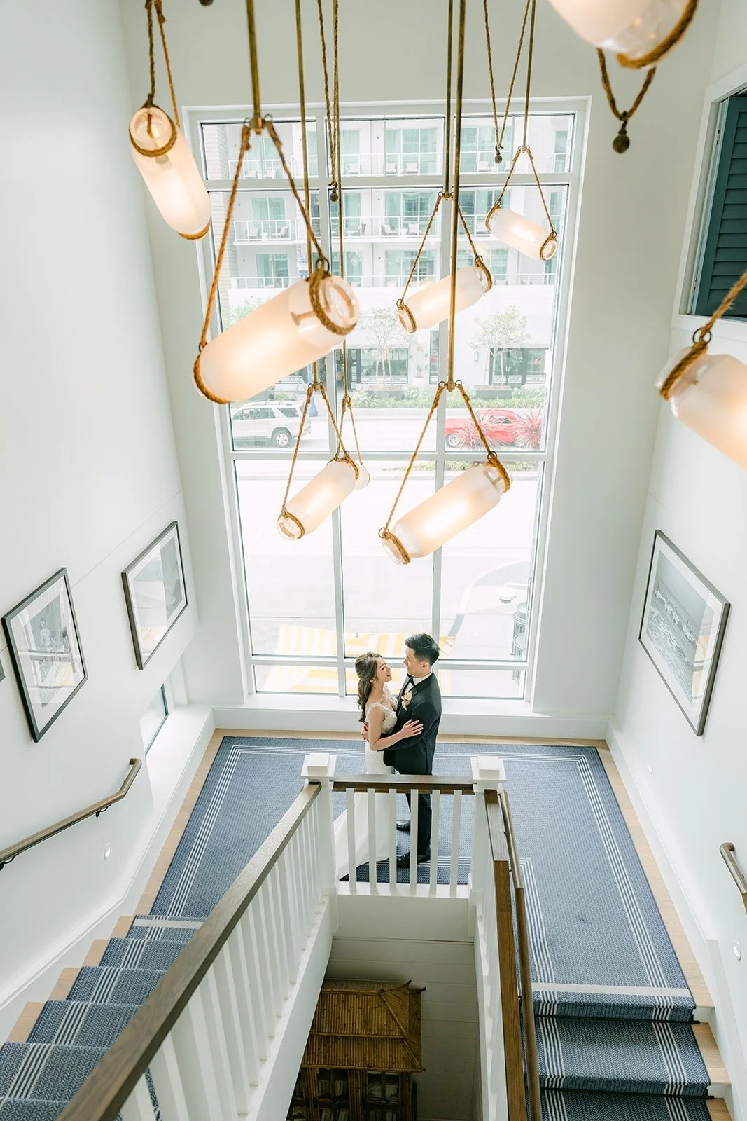 Angela and Eli on the staircase under a cluster of glass pendant lights at The Seabird