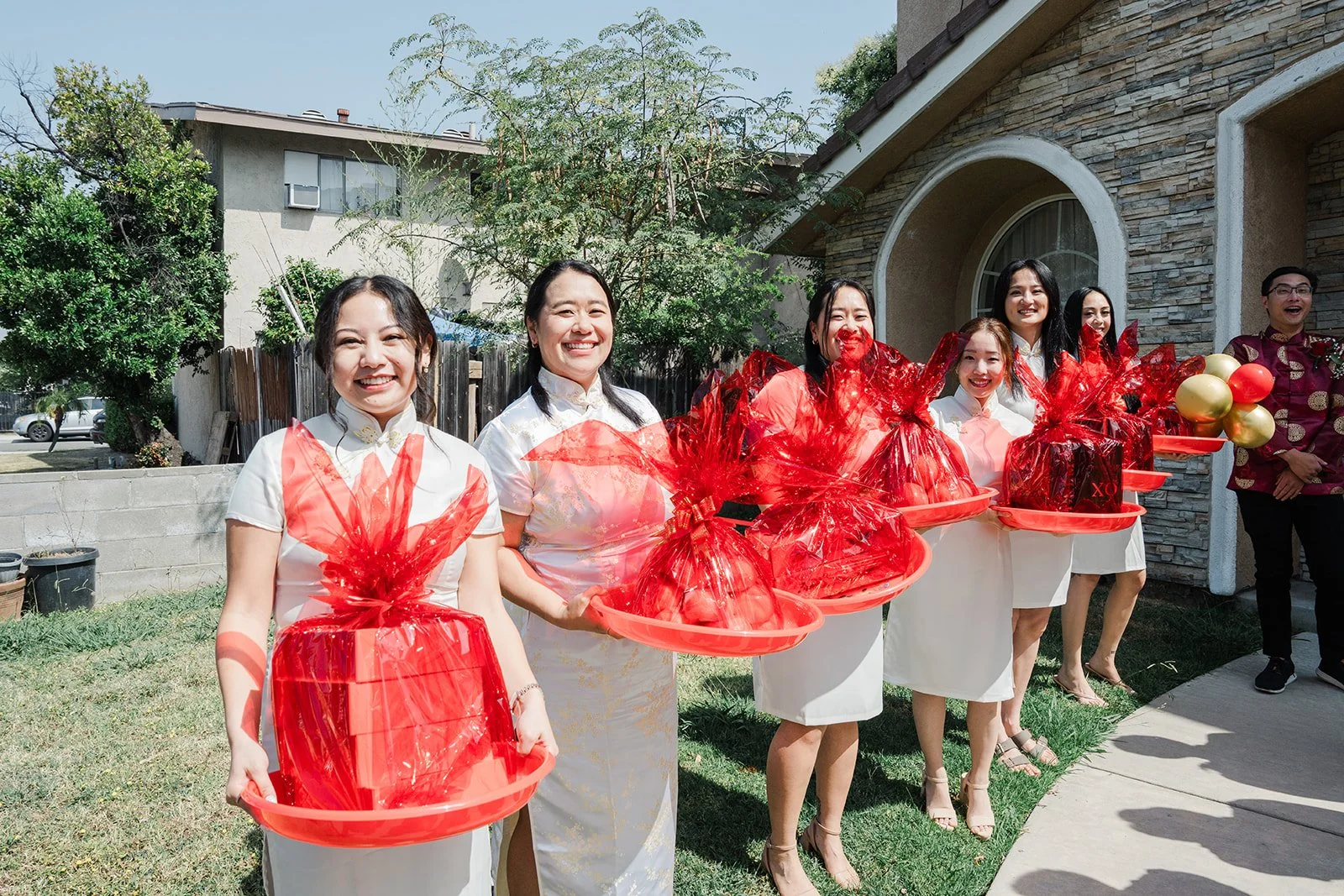 Bridesmaids holding red trays in front of the house, photographed by One and Only Production.