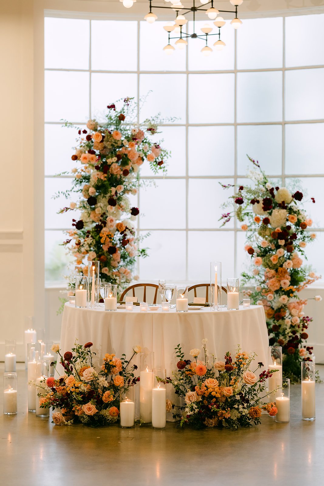 Sweetheart table framed by floral columns and candles in front of the window wall.