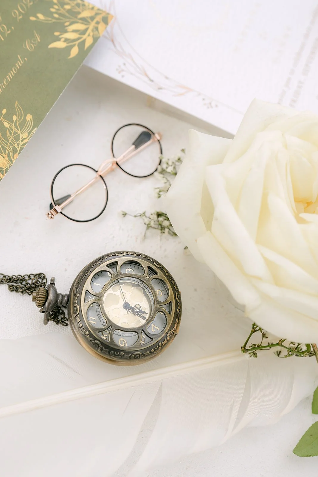 Round wire glasses and an antique pocket watch beside a white rose on the invitation suite