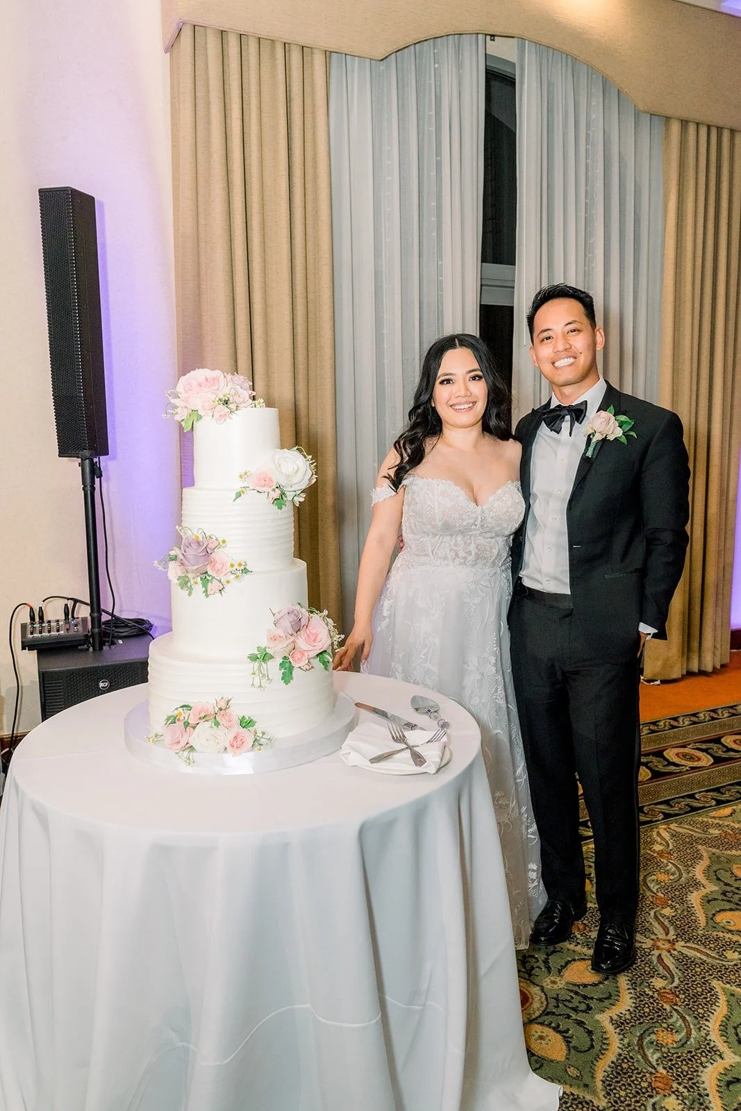 Francesca and Ralph beside their tiered white cake with pink florals