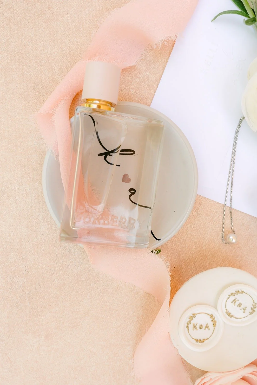 A perfume bottle and Kelli's earrings set beside a ribbon of blush silk