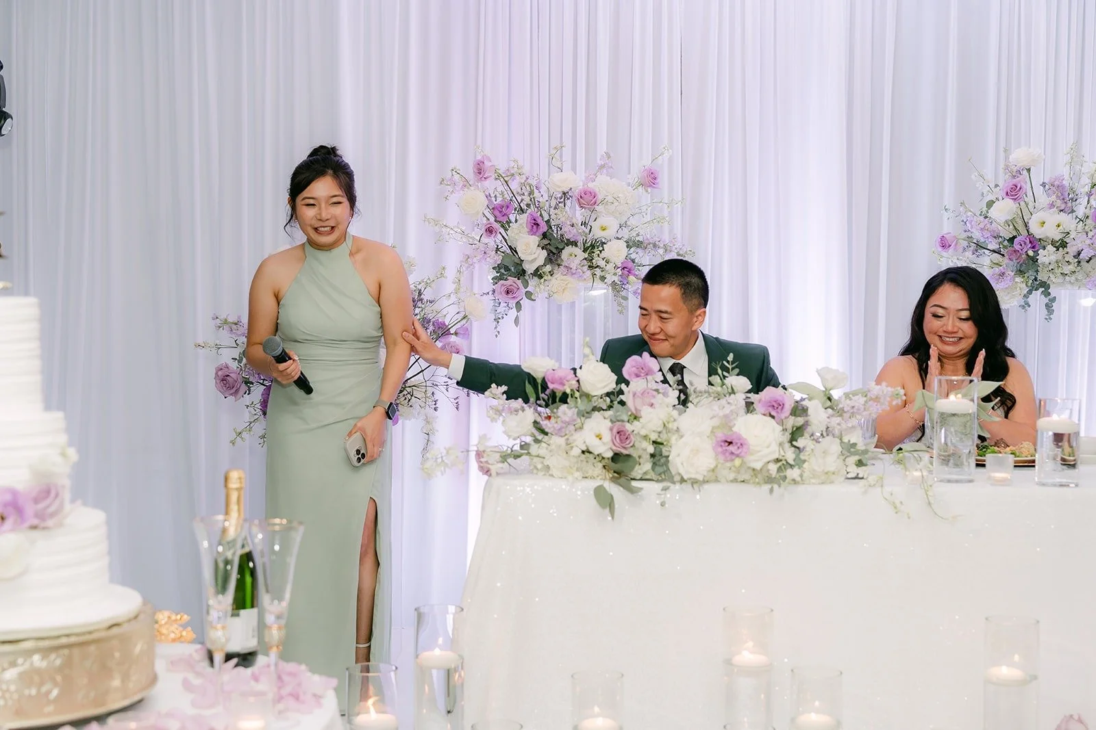 A bridesmaid in sage gives a speech as Jennifer and Kevin listen from the sweetheart table