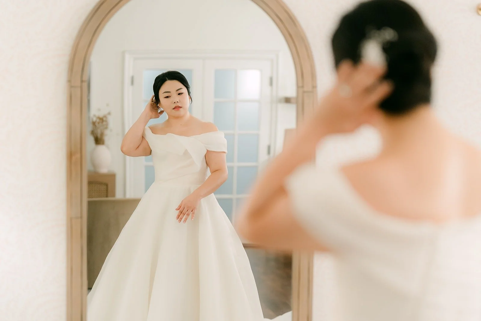 Chorok adjusting her hair in front of an arched mirror on her Franciscan Gardens wedding morning