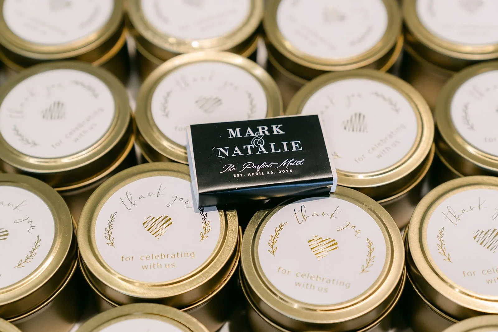 Gold lidded candle favors with a black matchbook reading Mark and Natalie